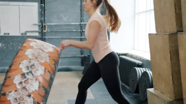 Silna dziewczyna podnosząca ciężką gumową oponę skoncentrowaną na treningu crossfit na siłowni — Wideo stockowe