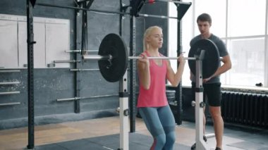 Spor giyim sektöründe narin bir kadın halterle spor salonunda koçla antrenman yapıyor.