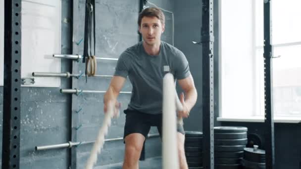 Porträt eines gutaussehenden Sportlers, der allein im Crossfit-Fitnessstudio gegen Seile kämpft — Stockvideo