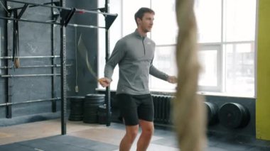 Spor salonunda ip atlamakla yakışıklı sporcu. Kardiyo egzersizine odaklanmış.