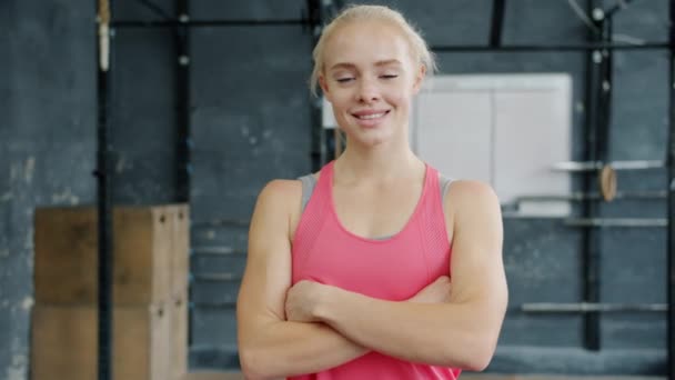 Porträtt av glad ung blond idrottskvinna som står i gymmet ensam och ler — Stockvideo