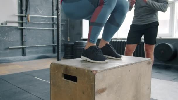 Plan bas de la sportive sautant sur la boîte en bois pendant l'entraînement Crossfit avec l'entraîneur — Video