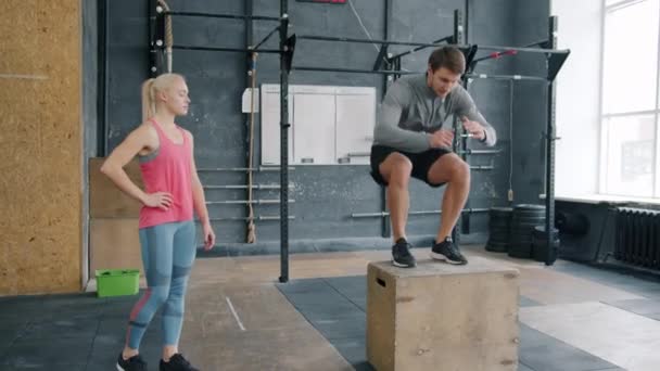 Fiatal férfi ugrás a fadobozon a cross fit edzés közben, miközben a női edző figyel — Stock videók
