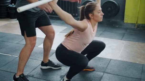 Inclinaison de fille en forme accroupi avec barre lourde exercice à l'intérieur dans la salle de gym avec entraîneur — Video