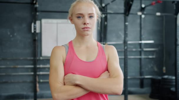 Портрет красивої блондинки в спортивному вбранні, що стоїть в спортзалі з серйозним обличчям і дивиться на камеру — стокове відео