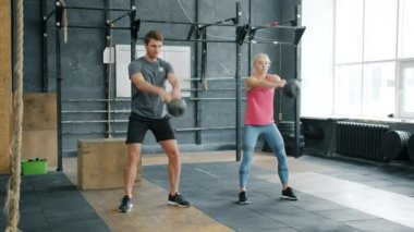 Spor salonunda kadın ve erkek antrenman yapıyor. Kettlebell 'le çömelmiş antrenmanlara odaklanıyor.