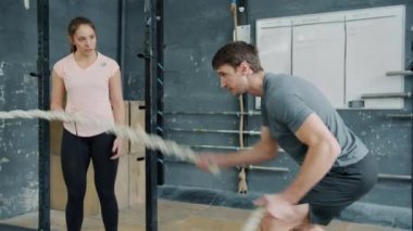 Modern Crossfit jimnastik salonunda antrenörle antrenman yapan sporcu adam yavaş hareket ediyor.