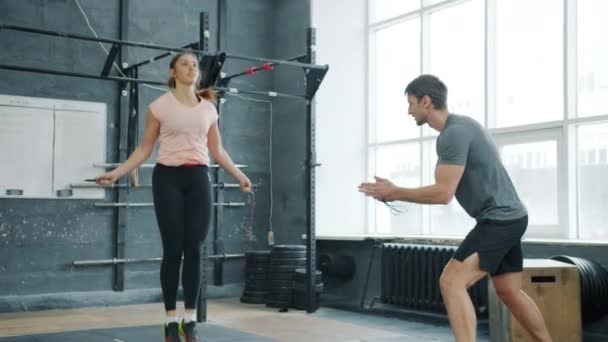 Porträt eines jungen Mädchens, das mit Springseil springt und eines Mannes, der eine Frau in der Turnhalle motiviert — Stockvideo