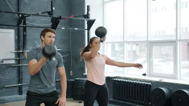 Menina e cara parceiros esportivos agachando e levantando kettlebells pesados trabalhando no ginásio juntos — Vídeo de Stock