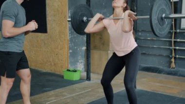 Spor salonundaki genç bayan halter haltercisiyle antrenman yapıyor.