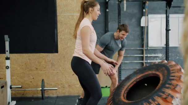 Trage beweging van vrouwentraining in de fitnessruimte met rubberen bandenliftgewicht trainen met trainer — Stockvideo
