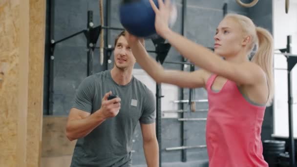 Lächelnder Trainer motiviert junge Frau beim Crossfit-Training, Mädchen wirft schweren Ball — Stockvideo