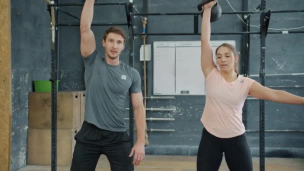 Mann und Frau stemmen gemeinsam Kettlebells-Training im Fitnessstudio — Stockvideo