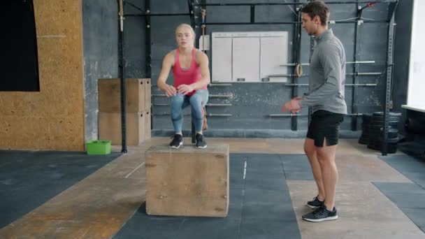 Menina em treinamento de roupas esportivas com treinador em ginásio fazendo crossfit caixa saltos concentrados em atividade — Vídeo de Stock