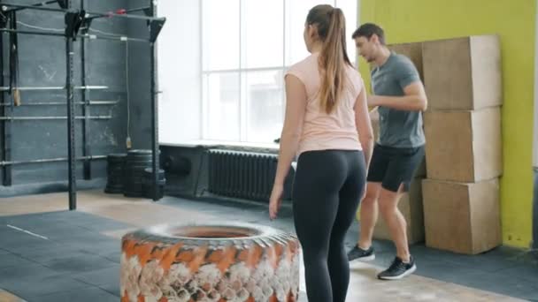 Rückenansicht des Sportlertrainings in Crossfit-Fitnessstudio mit Instruktor, der Reifen anhebt — Stockvideo