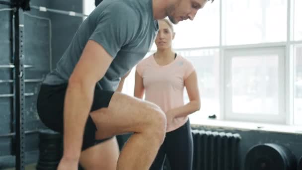 Fešák ve sportovním oblečení a tenisky skákání na dřevěné krabici školení s crossfit instruktorem v tělocvičně — Stock video