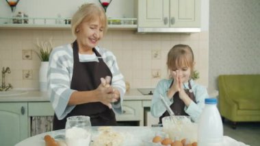 Yaşlı kadın ve küçük kızın portresi mutfakta yemek pişiriyor sonra hamur bıyığı yapıyor ve gülümsüyor.