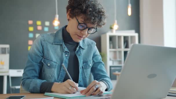 Atrakcyjna dziewczyna korzystająca z laptopa i robiąca notatki w biurze pracująca sama w kreatywnym miejscu pracy — Wideo stockowe
