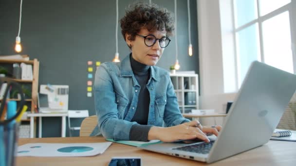 Ciddi bir kadın yaratıcı ofiste dizüstü bilgisayar kullanıyor. Masada tek başına çalışıyor. Bilgisayarlara odaklanıyor. — Stok video