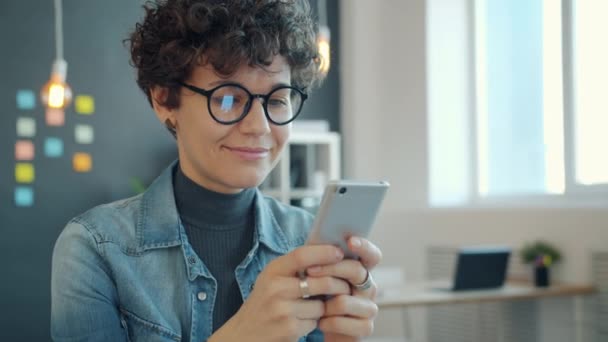Akıllı telefon kullanan gülümseyen kız iş yerinde sosyal medya iletişiminin keyfini çıkarıyor — Stok video