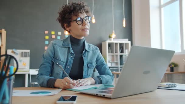 Жінка-підприємець пише за столом в офісі, працюючи самостійно плануючи бізнес — стокове відео