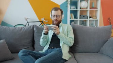 Mutlu genç adamın portresi akıllı telefon kullanarak evde oyun oynayarak eğleniyor.