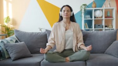 Kulaklık takmış, müzik dinleyen ve Lotus pozisyonunda dinlenen mutlu bir kız.
