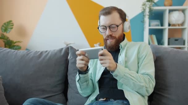 Câmera lenta de cara feliz usando fones de ouvido jogando jogo de vídeo sozinho em estúdio — Vídeo de Stock