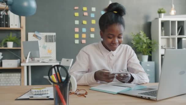 Χαρούμενη μικτή φυλή κορίτσι παίζει κινητό video game απολαμβάνοντας δροσερό εφαρμογή στο γραφείο — Αρχείο Βίντεο