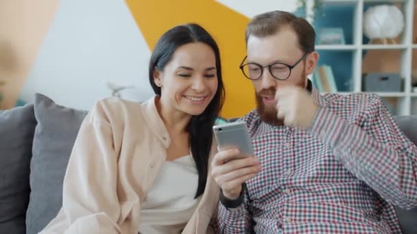 Мужчина и женщина с помощью смартфона смотрят на экран и смеются, наслаждаясь контентом — стоковое видео