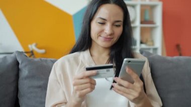 İnternetten alışveriş yapan neşeli kızın elinde banka kartı ve akıllı telefon tutması.