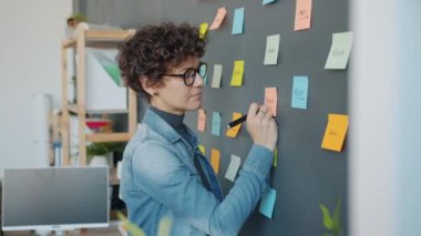 Ofis duvarına yapışkan notlar yazan kız iş yerindeki yaratıcı projeye odaklanmış.