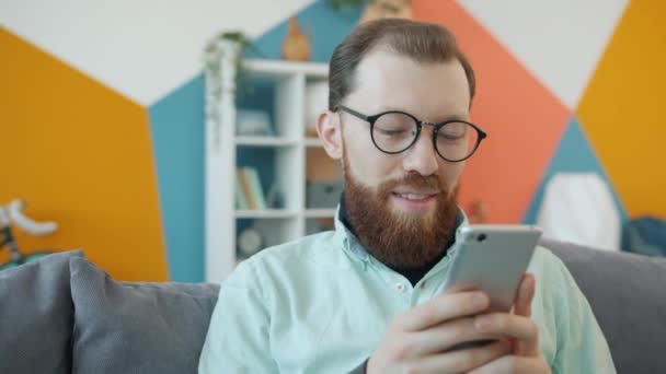 Aantrekkelijke kerel genieten van sociale media met smartphone aanraken scherm in appartement — Stockvideo