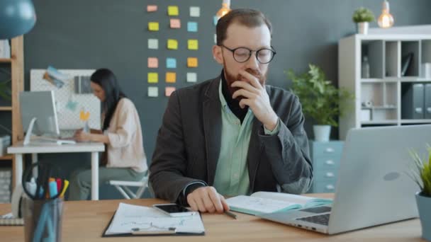 Бізнесмен застрягає за столом на роботі, а потім прокидається, працюючи з ноутбуком, колега зайнятий у фоновому режимі — стокове відео