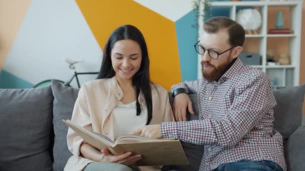 Hombre y mujer leyendo libro juntos hablando y disfrutando del tiempo libre en casa — Vídeos de Stock