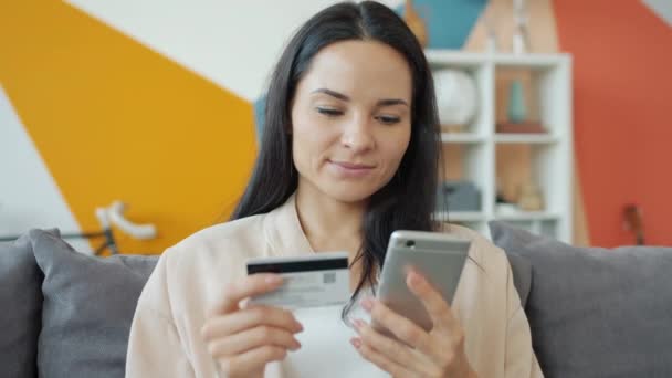 Junge Frau zahlt bargeldlos online mit Kreditkarte und Smartphone in Wohnung — Stockvideo