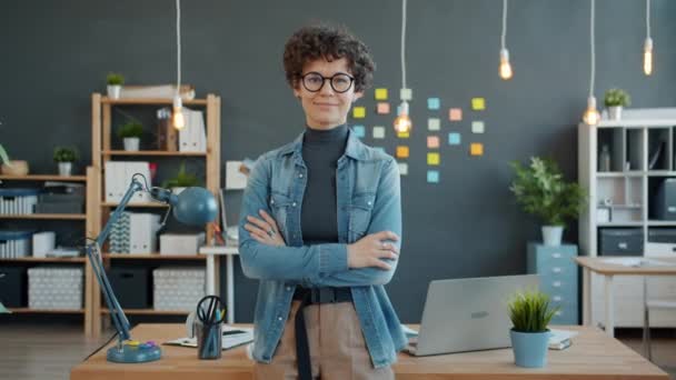 Ritratto di ragazza attraente in piedi in ufficio sorridente guardando la macchina fotografica che indossa occhiali e abbigliamento alla moda — Video Stock