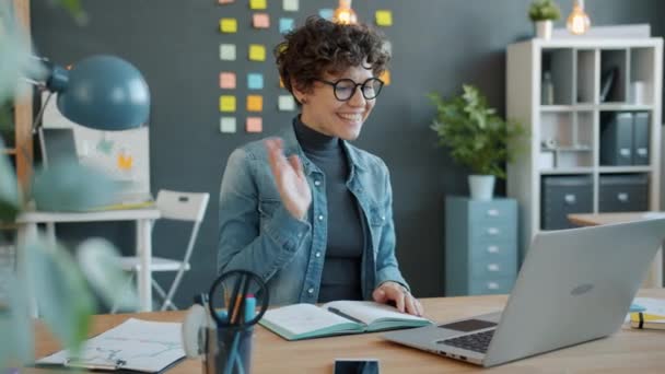 Повільний рух радісної бізнес-леді, що виступає на відеодзвінку з ноутбуком на робочому місці — стокове відео