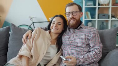 Genç kız ve erkek birlikte TV seyrediyor. Konuşuyor ve gülüyorlar. Evde eğleniyorlar.