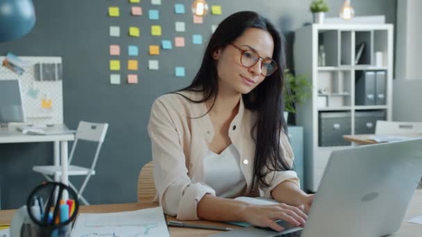 Mooie vrouw werken met laptop en schrijven in notebook geconcentreerd op baan in kantoor — Stockvideo