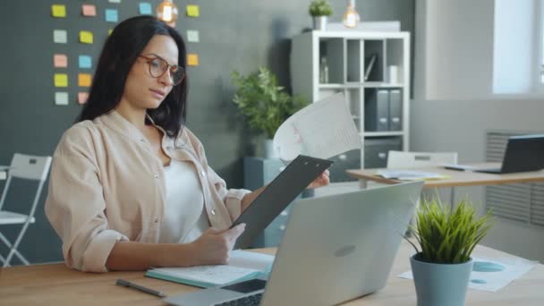 Üzletasszony nézi dokumentum és laptop képernyő összpontosított munka az irodában — Stock videók