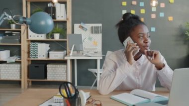 İşte cep telefonuyla konuşan neşeli melez kız ofiste masa başında oturuyor.