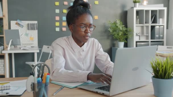 Уставшая девушка смешанной расы, использующая ноутбук и страдающая головной болью в креативном офисе — стоковое видео