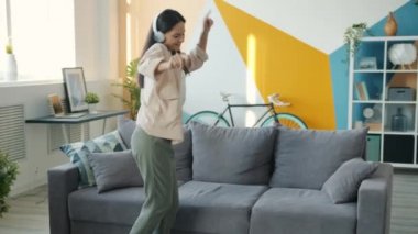 Kablosuz kulaklıklı neşeli genç kadın dans ederek eğleniyor.