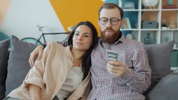 Hombre y mujer viendo la televisión sentados en el sofá juntos sosteniendo el control remoto — Vídeos de Stock