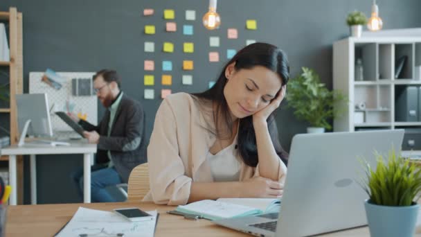 Mujer cansada durmiendo en la oficina y luego trabajando con el ordenador portátil en la oficina, colega ocupado en segundo plano — Vídeos de Stock