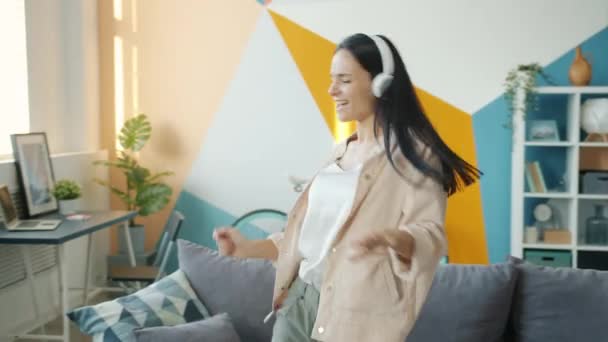 Chica feliz en los auriculares bailando en el apartamento con auriculares inalámbricos — Vídeos de Stock