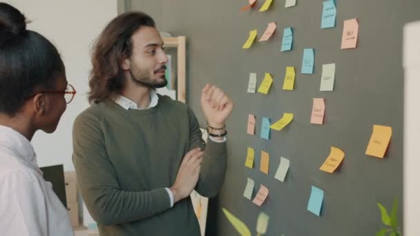 Mouvement lent du mec arabe et de la fille afro-américaine travaillant avec des notes collantes au bureau — Video