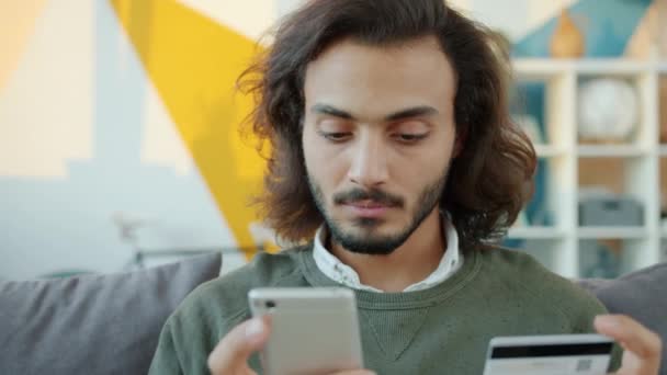 Sério cara árabe compras on-line pagando com cartão bancário e smartphone de casa — Vídeo de Stock