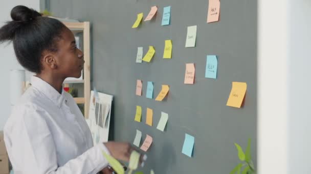 Movimiento lento de la mujer de negocios afroamericana que trabaja con notas adhesivas en la pared de la oficina — Vídeo de stock